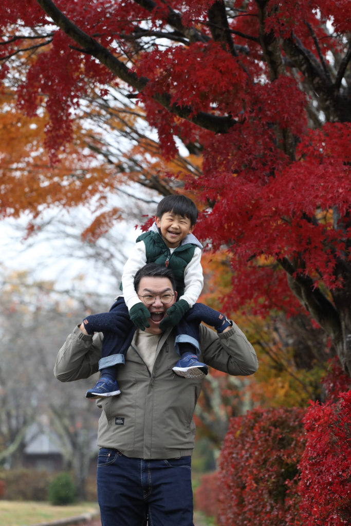 120 Child sitting on father’s shoulders in front of red autumn foliage